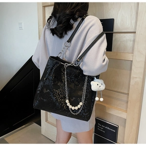 Detail of black snake-embossed tote bag featuring metallic chains and pearl ornaments