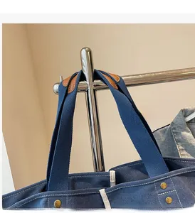 Detail of navy canvas tote bag featuring brown leather handles and golden metal rivets