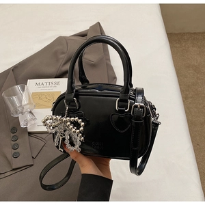 Detail of black glossy handbag with silver heart hardware and beaded bow charm accessory