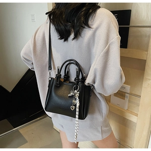Detail of black lychee grain bucket bag with silver heart charm and woven strap accents
