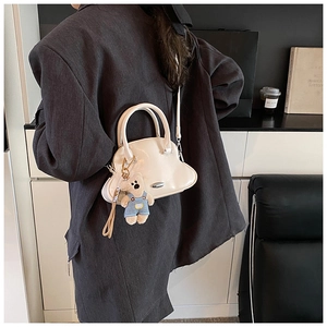 Bolso tipo concha beige con colgante de osito de peluche y acabado brillante