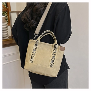 Detail view of beige canvas tote with Gentlewoman logo straps and leather trim accents