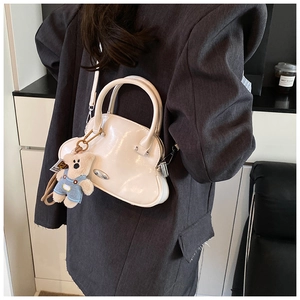 Elegante bolso de concha blanco crema con acabado brillante y adorno de oso