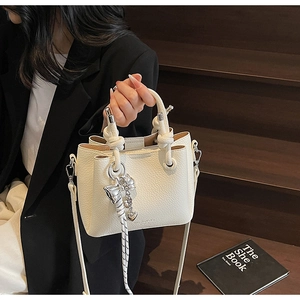 Detail of white lychee leather bucket bag with knot handle and silver bow heart charms