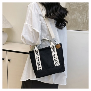Detail of black canvas tote bag with Gentlewoman logo strap worn by a model