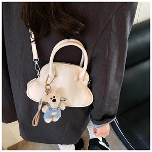 Detalle de bolso de concha crema con colgante de oso de peluche sobre blazer gris oscuro