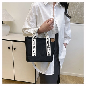 Detail of black canvas tote bag featuring branded white webbing handles and slim shoulder strap