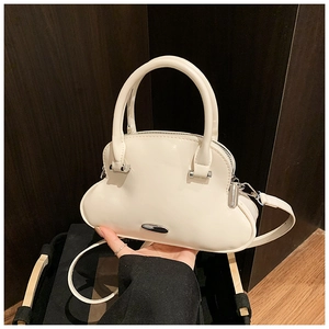 Detalle del bolso de mano crema con forma de nube y cremallera plateada de acabado liso
