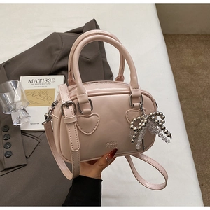 Close-up of pink patent leather handbag with heart patch, COIN 2DN logo and bow charm