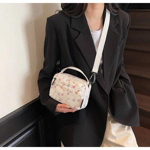 Close-up of white floral patterned fabric texture and metal strap hooks on a small crossbody bag