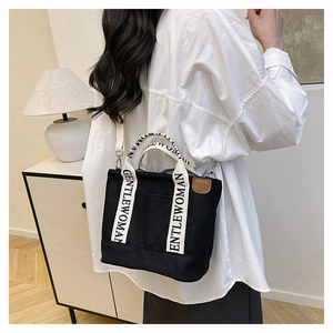 Detail of black canvas tote bag showing white GENTLEWOMAN strap and silver metal buckle