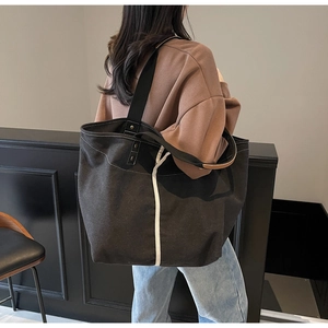 Detail of a black canvas tote bag with white stripes and brown leather handles on shoulder