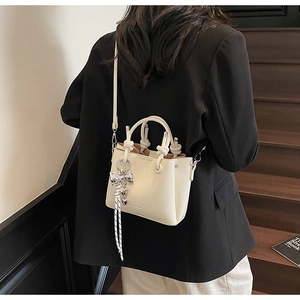 Detail of off-white bucket bag with knot handle and silver butterfly heart charms