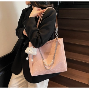Detail of pink snake-embossed tote bag featuring a pearl chain and cloud plush charm