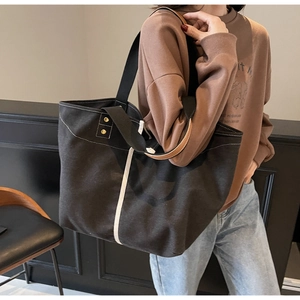 Close-up of black tote bag with brown leather handles and white stripe detail