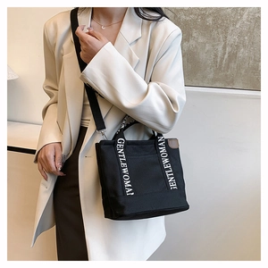 Detail of black canvas tote bag showing GENTLEWOMAN strap and adjustable shoulder strap