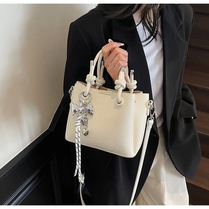 Detail of cream bucket bag with knotted rope handle and silver bow heart charms