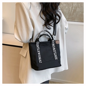 Detail view of the black canvas tote bag worn by a model in a stylish white blazer