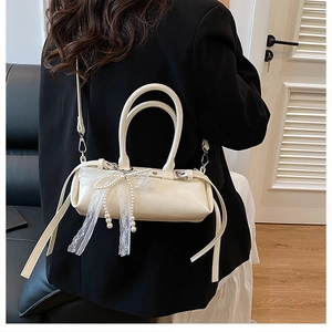 Dettaglio borsa baguette crema con fiocco in pizzo e perle indossata su un blazer nero