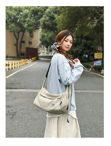 Detail view of a beige canvas messenger bag with wide black strap in casual outdoor use