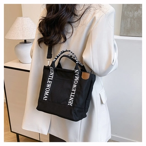 Detail of black canvas tote bag with GENTLEWOMAN logo strap and brown leather patch