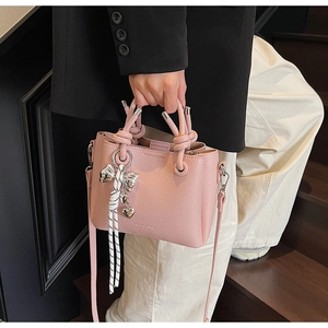 Detail of pink lychee leather bucket bag featuring knot handles and a metal bow charm