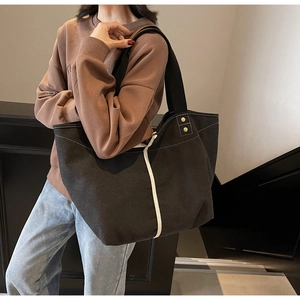 Detail of black canvas tote bag with contrast white stitching and gold metal rivets