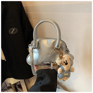 Detalle de bolso plateado metalizado con textura arrugada y colgante de oso de peluche