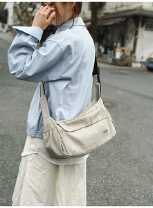 Detail of beige nylon crossbody bag featuring adjustable black strap and side pocket