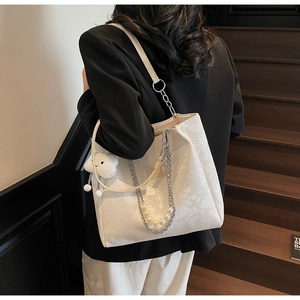 Detailed shot of white faux snakeskin tote with silver chain, pearls, and cloud charm