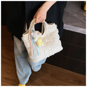 Détail du sac seau blanc texturé avec un charm d'ours en peluche et glands colorés