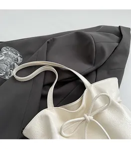 Détail du cabas plissé blanc avec décoration de nœud sur un fond de costume gris