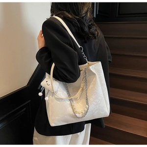 Detail of white snakeskin tote bag featuring pearl chain and fuzzy cloud pendant