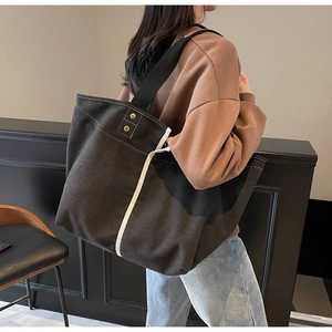Side view of a large black canvas tote bag with white trim worn by a model in casual wear