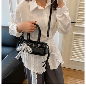 Dettaglio della borsa Boston in pelle nera con fiocco in pizzo bianco e ciondolo di perle
