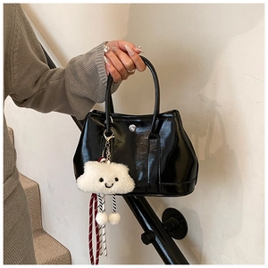 Detail of glossy black patent leather handbag featuring a white plush cloud charm accessory
