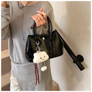 Detail view of black patent leather handbag with a plush white cloud charm and top handle