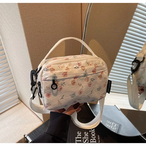 Detail of floral lace crossbody bag with zipper closure and brand tag on textured fabric
