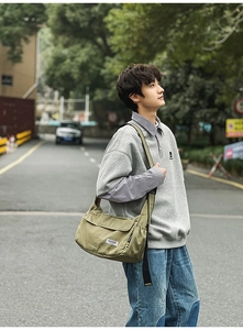 Outdoor shot of olive green canvas messenger bag with wide nylon strap and woven label