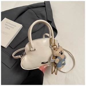 Detalle del bolso de mano color crema con colgante de osito sobre fondo de traje gris