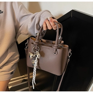 Detail of lychee pattern leather bucket bag with decorative bow and handle knots