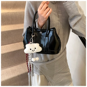 Detail of glossy black patent leather handbag with a cute white cloud plush pendant charm