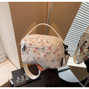 Close-up of floral lace texture, wide shoulder strap and circular zipper on the crossbody bag