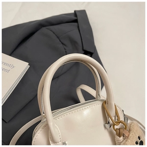 Detalle de bolso tipo concha en cuero crema con colgante de oso y herrajes metálicos
