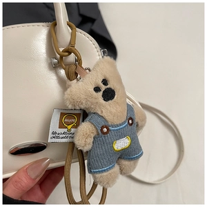 Colgante de oso de peluche con peto vaquero en un bolso de mano blanco