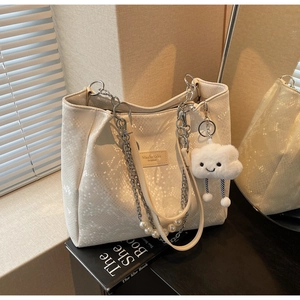 Detail of cream tote bag with snake texture, pearl chain, and plush cloud charm decor