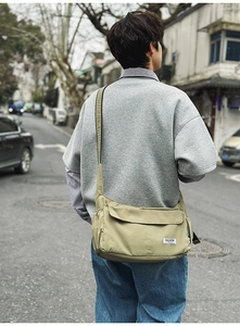 Rear view of a sage green nylon crossbody dumpling bag worn by a model in the city