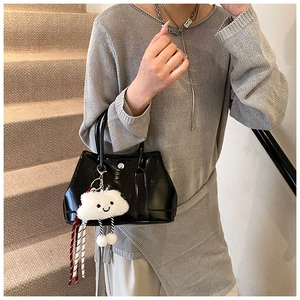 Close-up of black glossy leather tote bag with cute white plush cloud charm on a stair