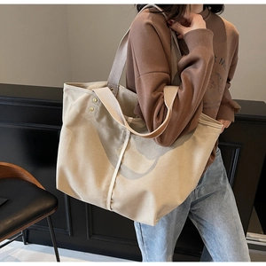 Detail view of large beige canvas tote bag with leather trim handles and gold rivets
