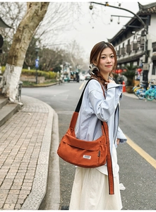 Detailed shot of a rust-orange nylon crossbody bag featuring a side drawstring pocket